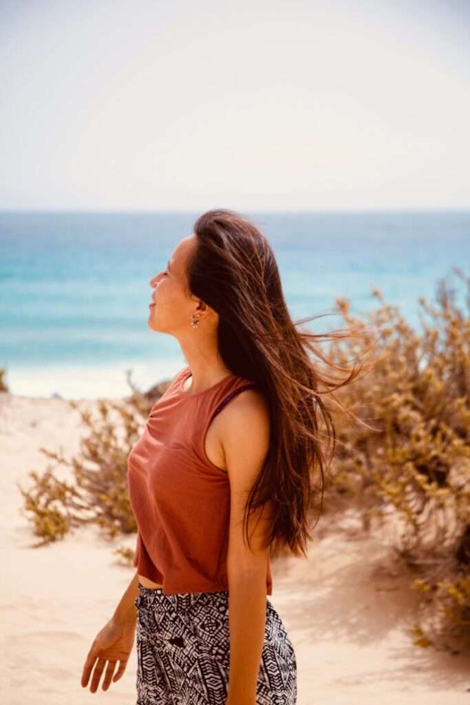 junizeit-Bloggerin Thuy-An befindet sich am Strand El Moro auf Fuerteventura und blickt in den Himmel. Im Hintergrund türkisfarbenes Meer.